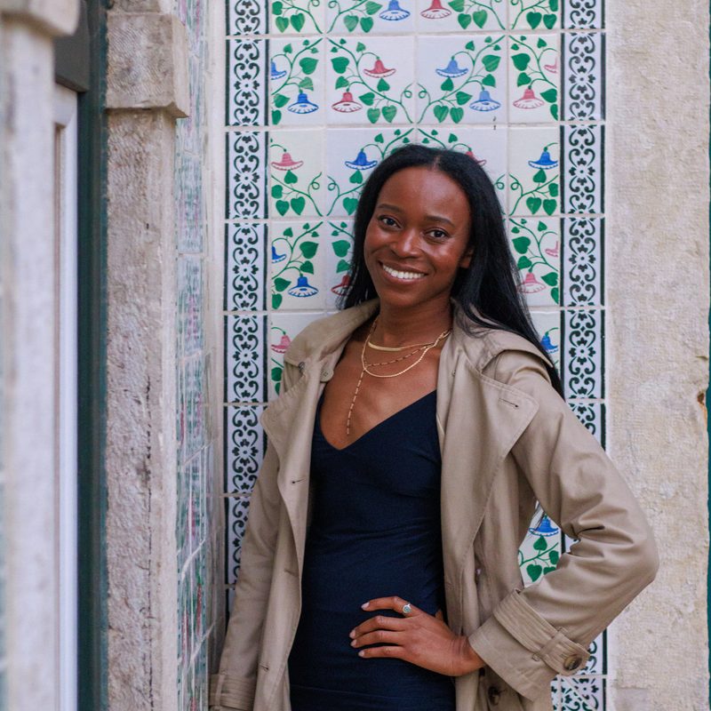 Stef Marie smiling in front of a tiled building facade in Lisbon, Portugal