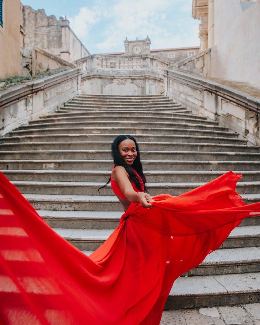 Stef Marie in a red dress on stone steps in Dubrovnik, Croatia